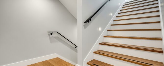 Remodeled basement stairs with wooden treads, white risers, black handrail, and bright recessed lighting in a finished stairwell.